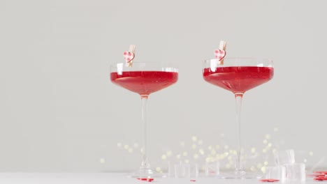 Video-of-red-drinks-in-two-cocktail-glasses-and-heart-shapes-on-white-background,-with-copy-space