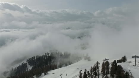 Snow-covered-pine-tree-forest-mountain-and-ski-lift-covered-in-low-fog-and-clouds