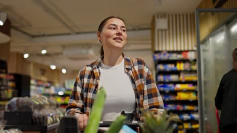 A-happy-brunette-girl-in-a-plaid-shirt-and-a-white-T-shirt-walks-along-the-shelves-and-inspects-goods-in-a-supermarket