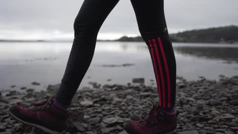 Slow-motion-of-a-person-walking-on-the-coast-of-a-lake-on-a-rocky-ground