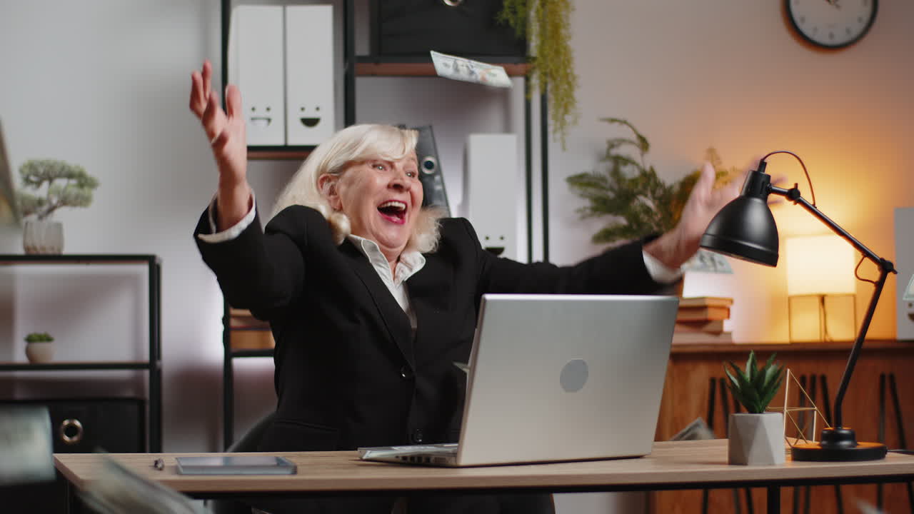 Money cash dollar rain falling on caucasian senior businesswoman using laptop at home office desk