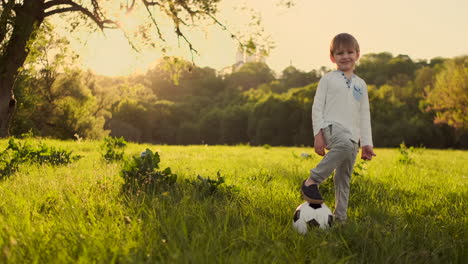 Junge-Steht-Im-Sommer-Mit-Einem-Fußball-Bei-Sonnenuntergang-Und-Schaut-In-Die-Kamera.