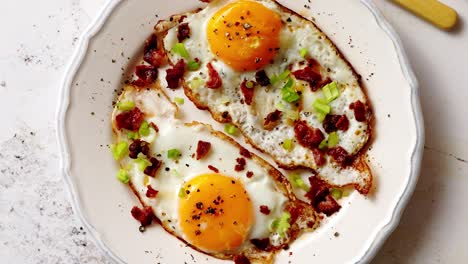 two fresh fried eggs with crunchy crisp bacon and chive served on rustic plate