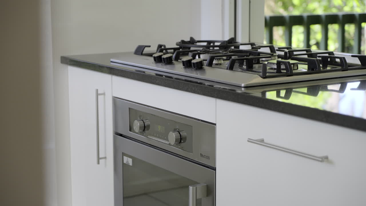 Primo piano di piano cottura a gas e forno, mobili da cucina bianchi, piano di lavoro in pietra.