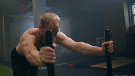 A-powerful-man-pushes-a-heavy-weight-trolley-in-the-gym-in-slow-motion.-Bearded-man-with-vapor-on-his-body-trains