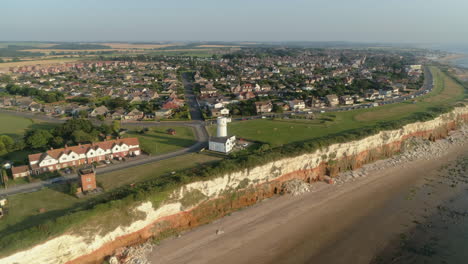 Hoch-Aufstellende-Luftdrohnenaufnahme,-Die-Sich-Um-Den-Alten-Leuchtturm-Von-Hunstanton-über-Orangefarbenen-Und-Weißen-Klippen-Und-Häusern-Mit-Kleinem-Sandstrand-Bei-Sonnenuntergang-Im-Norden-Von-Norfolk,-Großbritannien-Dreht