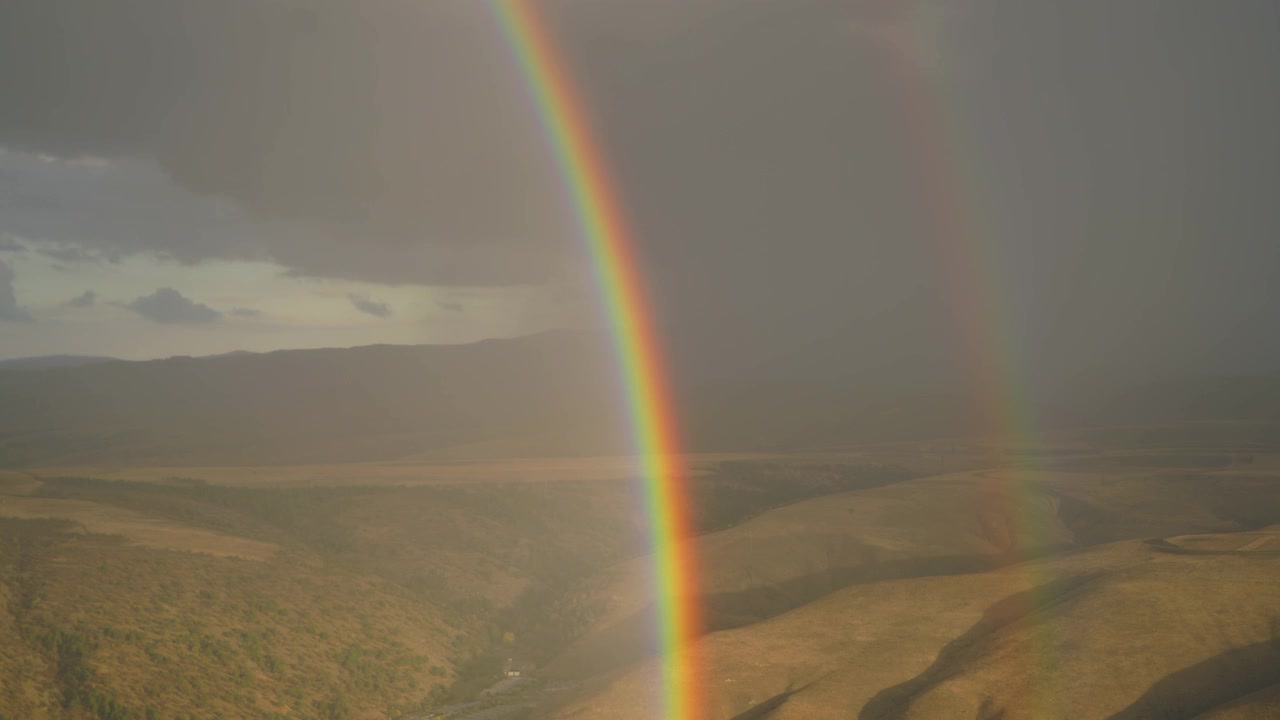 Double Rainbow Over Rolling Hills During Stormy Weather
