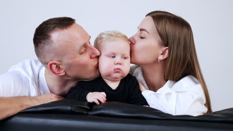 loving caucasian parents kiss their beloved blond baby on the cheeks. beautiful family portrait close up.