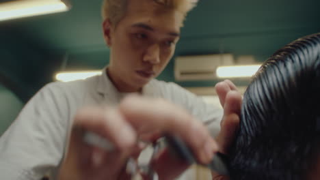 asian barber combing and trimming hair of client