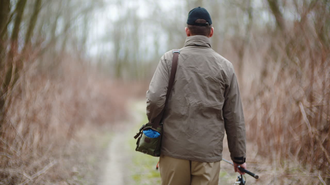 Man Holding Fishing Rod Walking Amidst Bare Trees