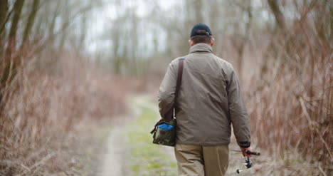 Man-Holding-Fishing-Rod-Walking-Amidst-Bare-Trees