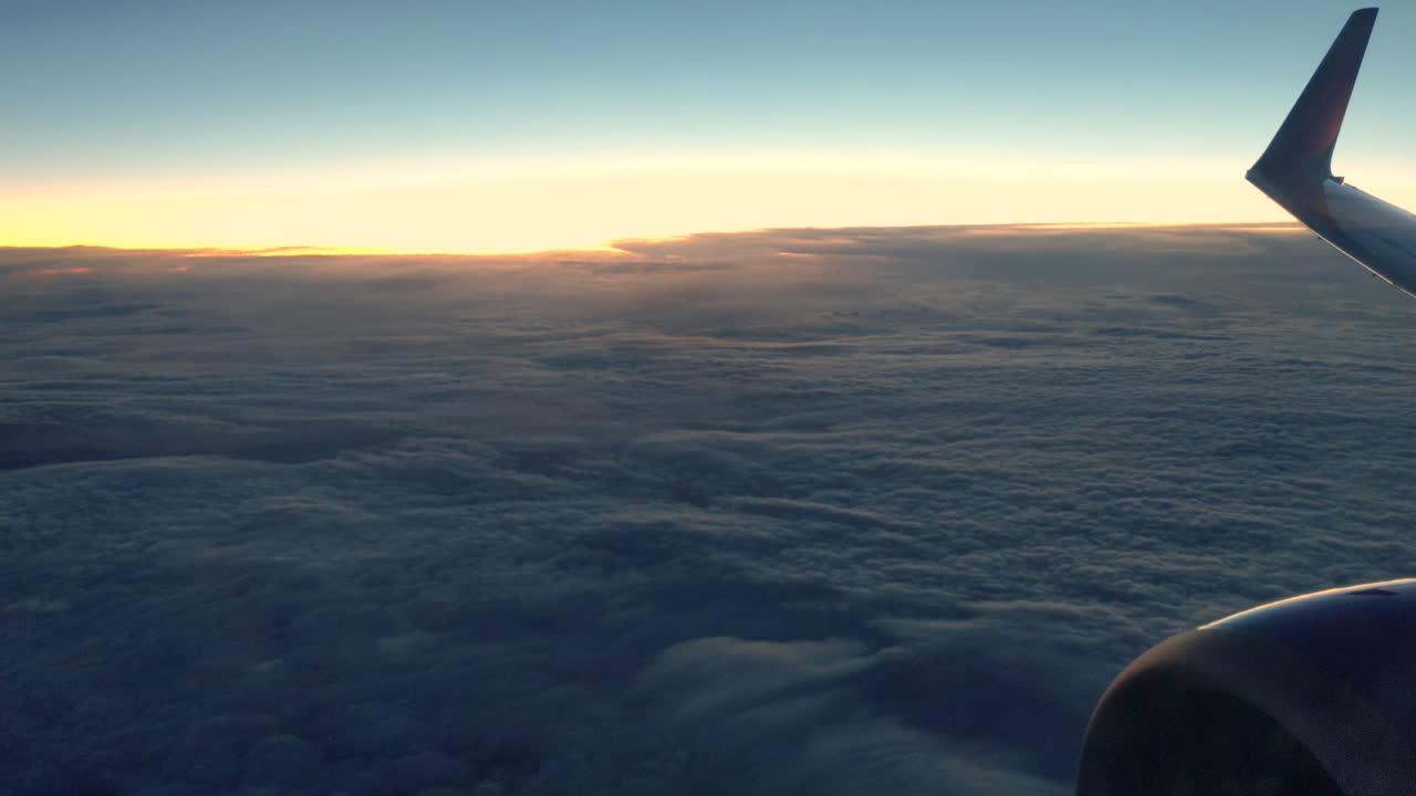Optagelse af en flymotor og vinge, der flyver over skyerne, mens solen går ned i horisonten
