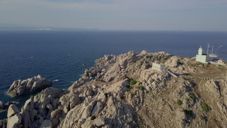 Un-Dron-Voló-A-Lo-Largo-De-La-Costa-Salvaje-Y-Rocosa-Del-Norte-De-Cerdeña-Para-Revelar-Una-Pequeña-Casa-De-Luz-Blanca-Con-Una-Bahía-Prístina-Detrás