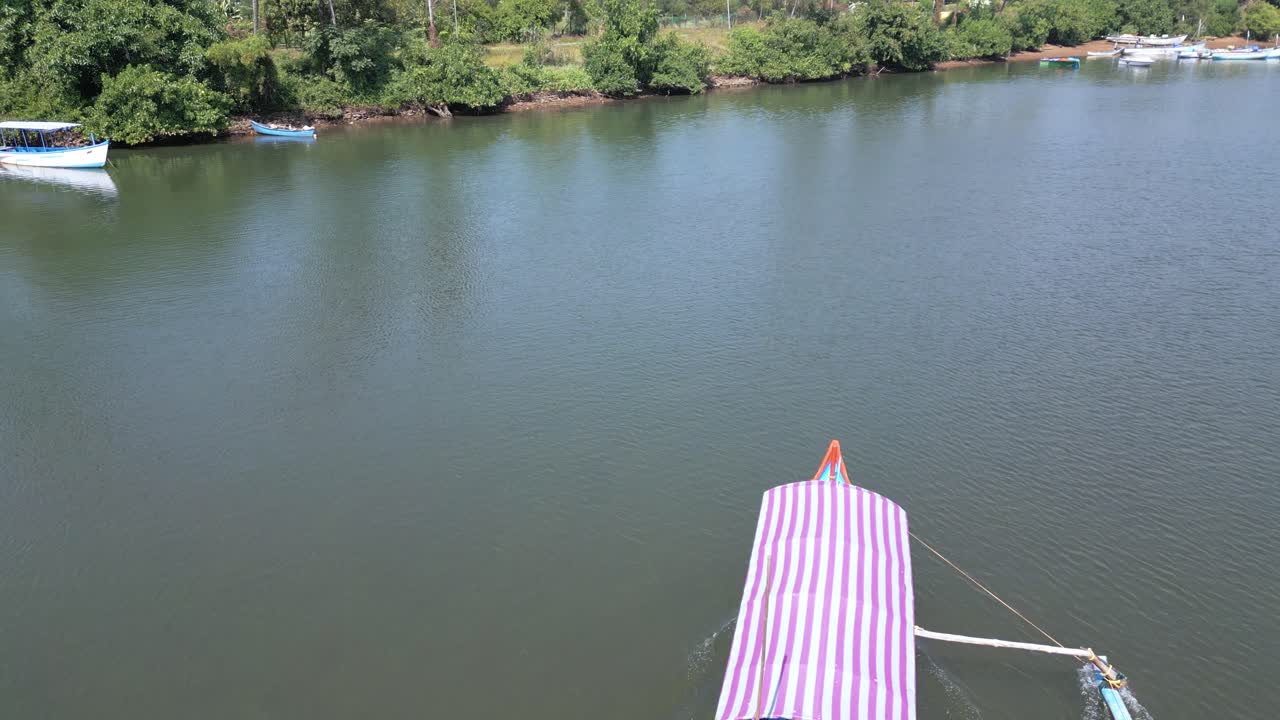 Close up drone view of a scenic boat trip along the Talpona River near Palolem Beach, Goa. Surrounded by lush green trees, the boat glides through calm waters under a bright, sunny sky
