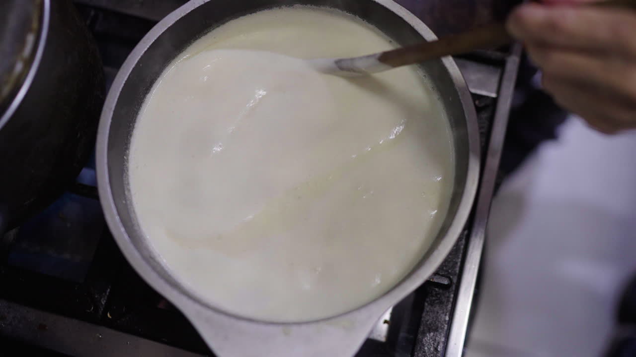 Creamy Bagna Cauda simmers as it’s stirred by hand in a modern kitchen, preserving a 16th-century Piedmontese ritual where farmers shared this anchovy-garlic sauce in warmth after vineyard labor.