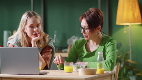 dos mujeres almorzando, hablando y usando una computadora portátil en casa