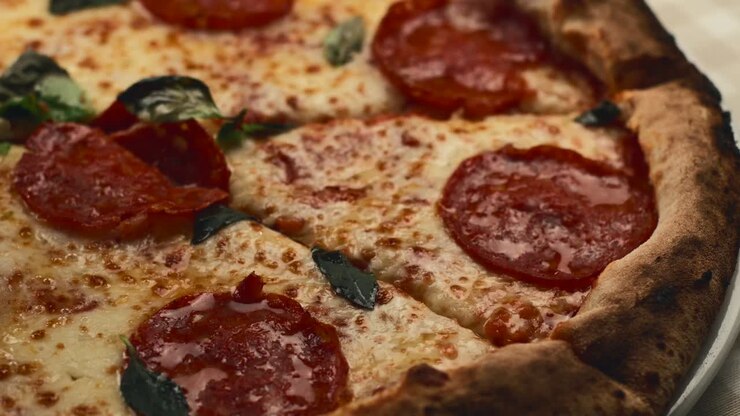 Primo piano di uno chef che taglia una pizza italiana appena sfornata, calda e gustosa