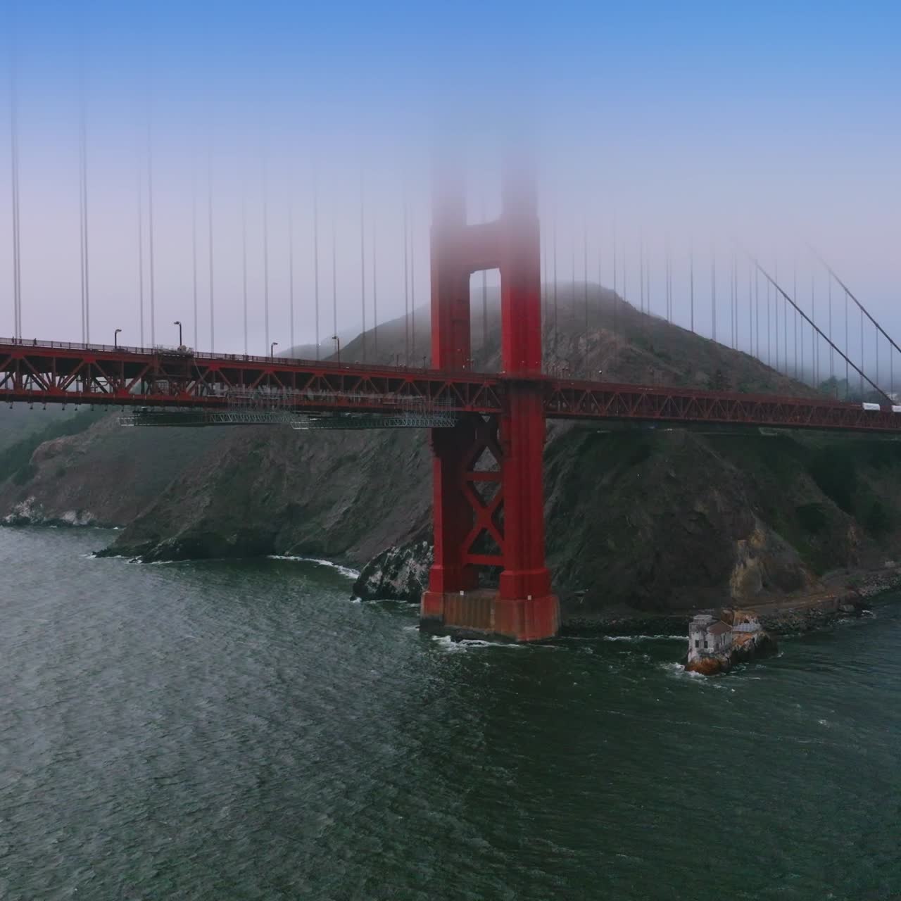 Part of beautiful famous Golden Gate Bridge at the backdrop of rocks. Hills and bridge tops hiding in the thick fog of San Francisco
