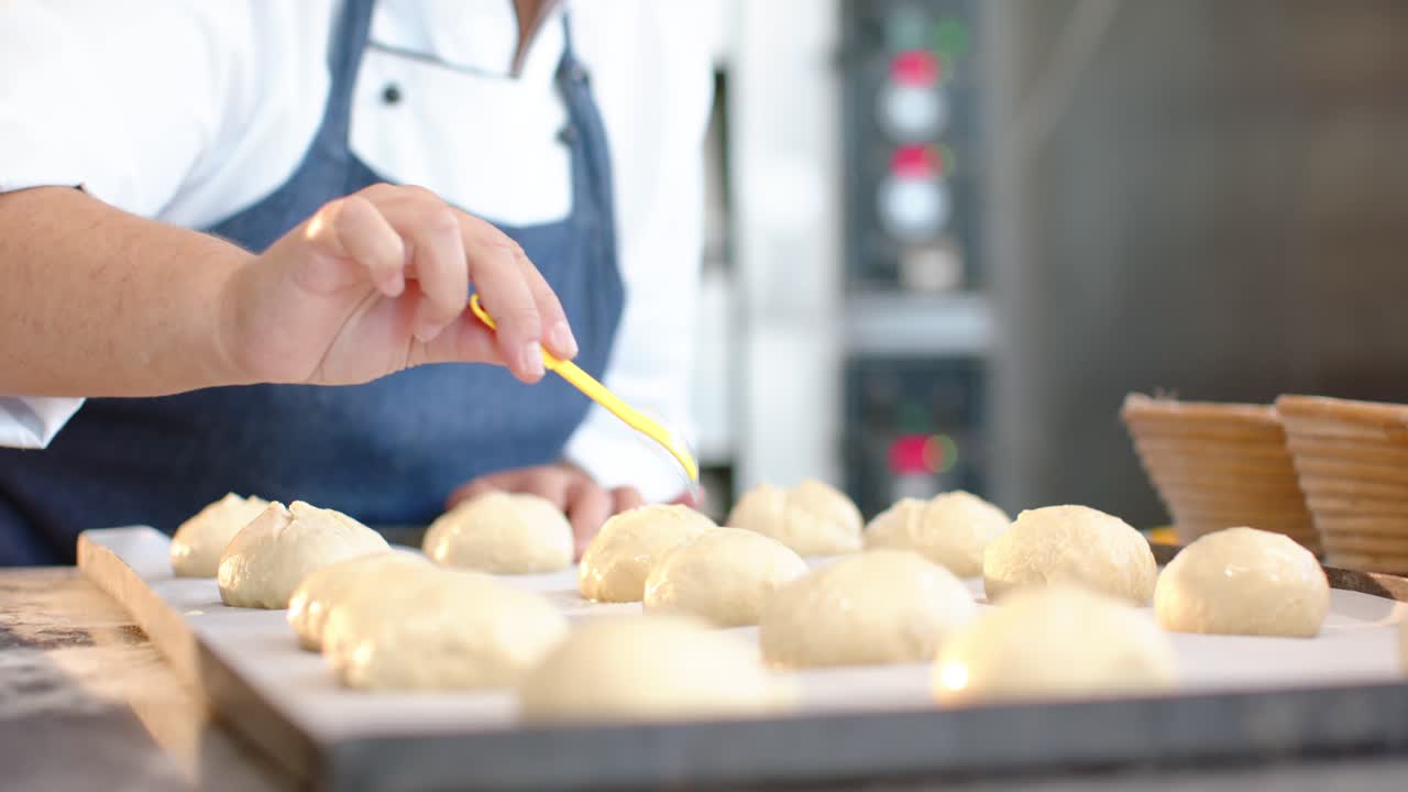 Female pastry chef reaching, brushing dough rows with yellow brush at bakery for baking, copy space