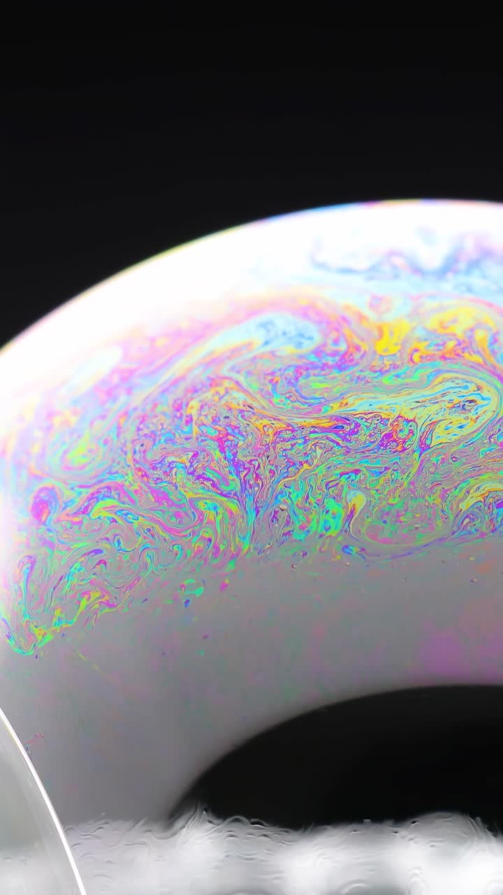 Colori vivaci e vorticosi sulla superficie di una bolla di sapone, catturati in primo piano con illuminazione dinamica e movimento fluido della telecamera.