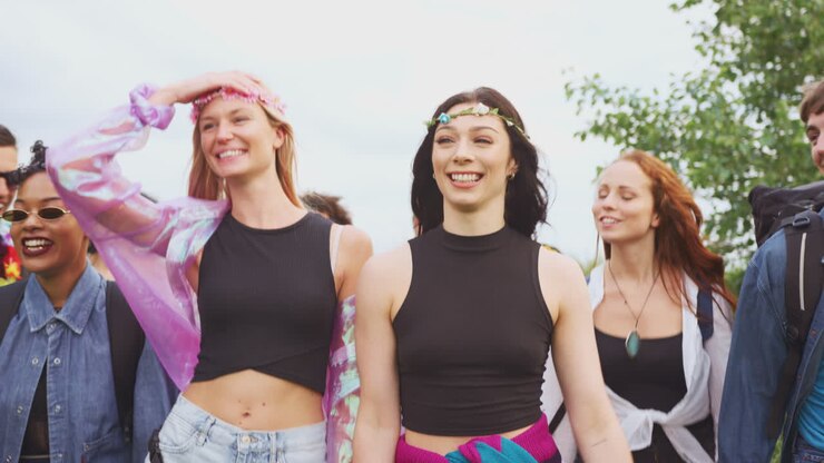 Gruppo di giovani amici entusiasti che trasportano attrezzatura da campeggio attraverso un campo per un festival musicale