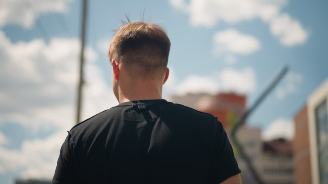 Молодой человек в белой куртке прогуливается по городу; городской пейзаж с идущим молодым человеком; молодой человек в белой куртке уходит по улице; юноша в белой одежде идет по оживленной городской улице