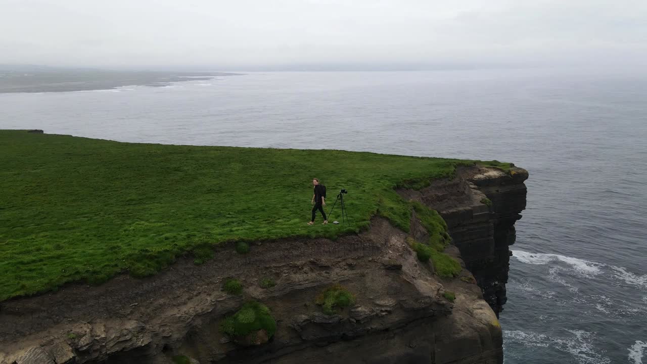 escena espectacular de una mujer fotografiando una enorme pila de mar en el condado de mayo irlanda con un trípode en el borde de un acantilado