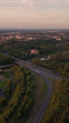 Aerial view of a highway and bridge surrounded by a lush green landscape with a distant city under a soft sky
