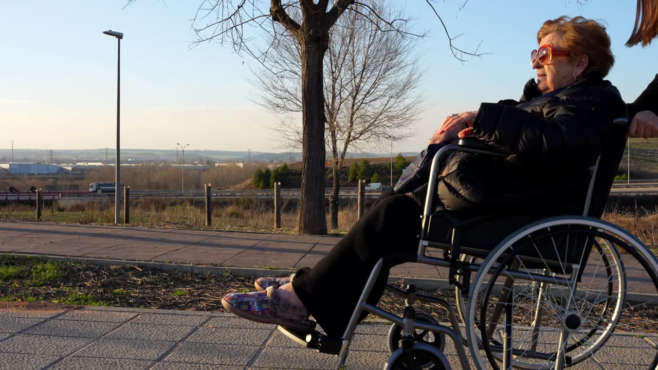 Old woman with sunglasses in a wheelchair being pushed by a young girl