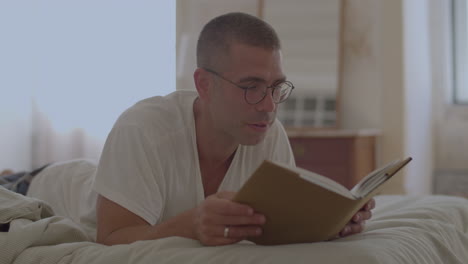 handsome man in eyeglasses reading book in bed in morning