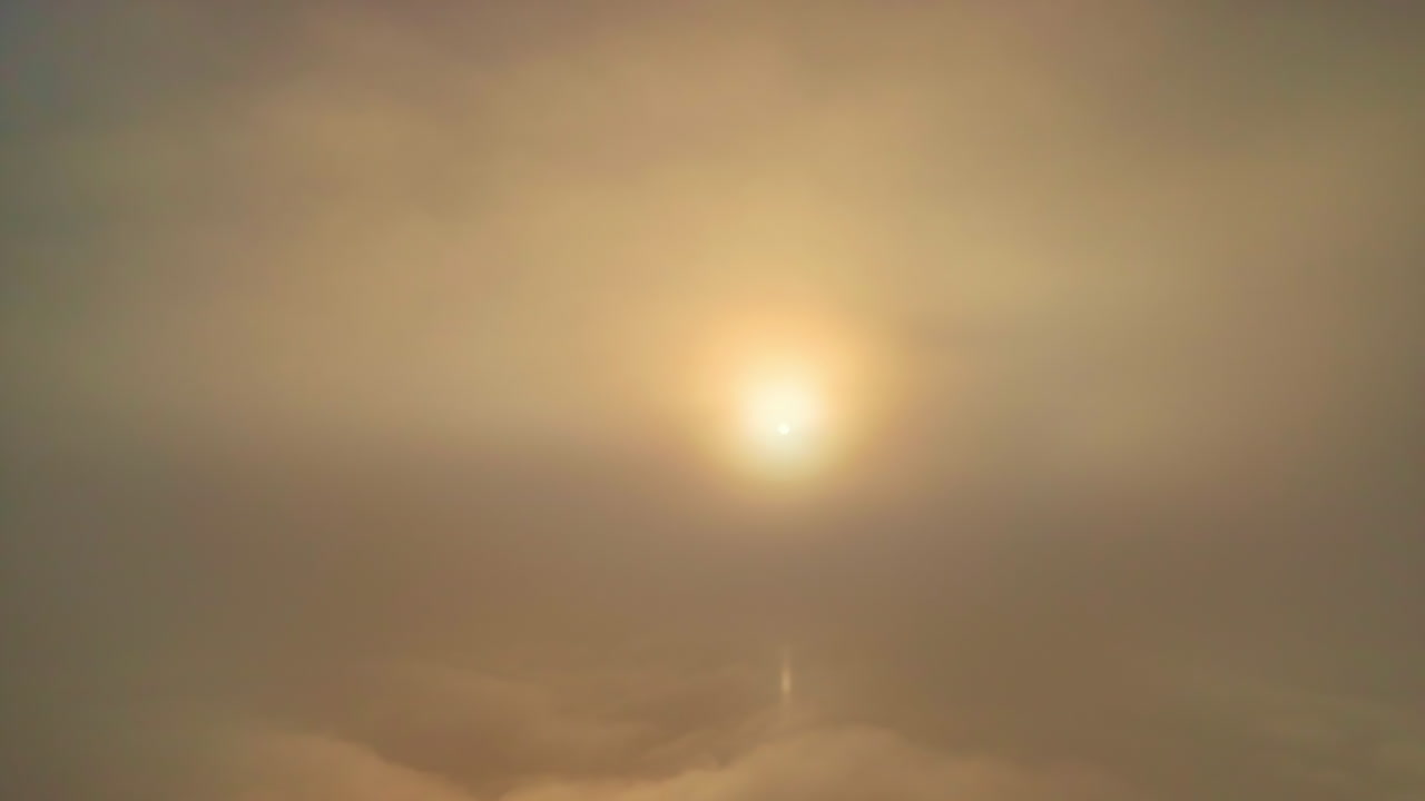 A radiant sun pierces through a gray mist and reveals a white cloud cover