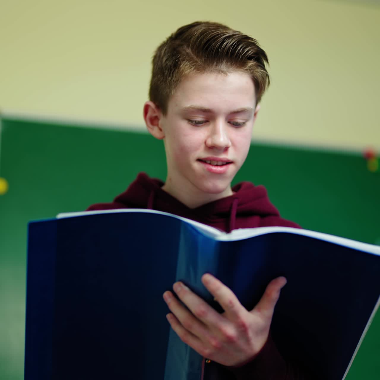 Boy looking into the school journal. Teenager standing in the classroom and reading information in the folder. Learning process at school.
