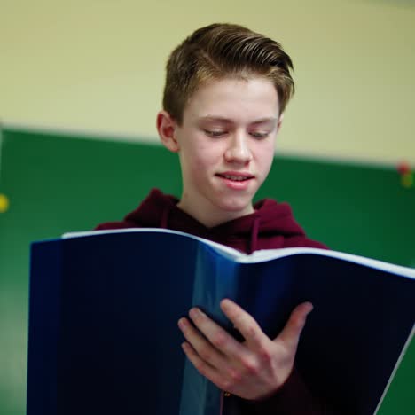 boy looking into the school journal. teenager standing in the classroom and reading information in the folder. learning process at school.