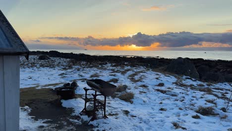 Panning-sunset-shot-from-Rolf's-Bar-in-Grunnfør,-Nordland,-Norway-near-Lofoten-with-snow-covered-shore,-birds-flying-and-a-coast-gaurd-boat-on-the-horizon