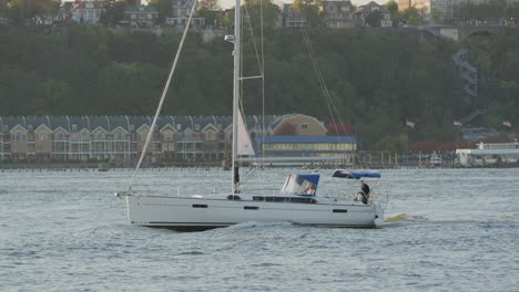 sailboat with single mast travelling along the hudson river during sunset with new jersey in the background