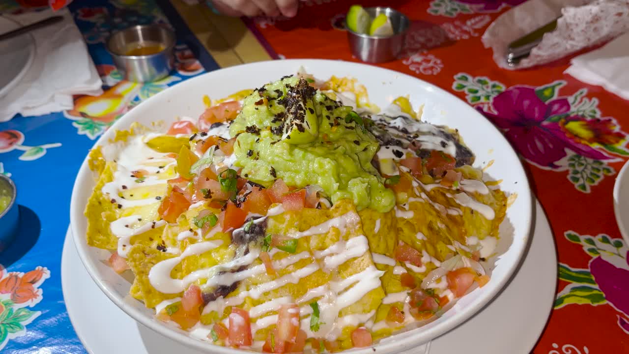 una vista de cerca de nachos cargados con queso derretido, pico de gallo fresco, guacamole y crema agria, cocina mexicana.