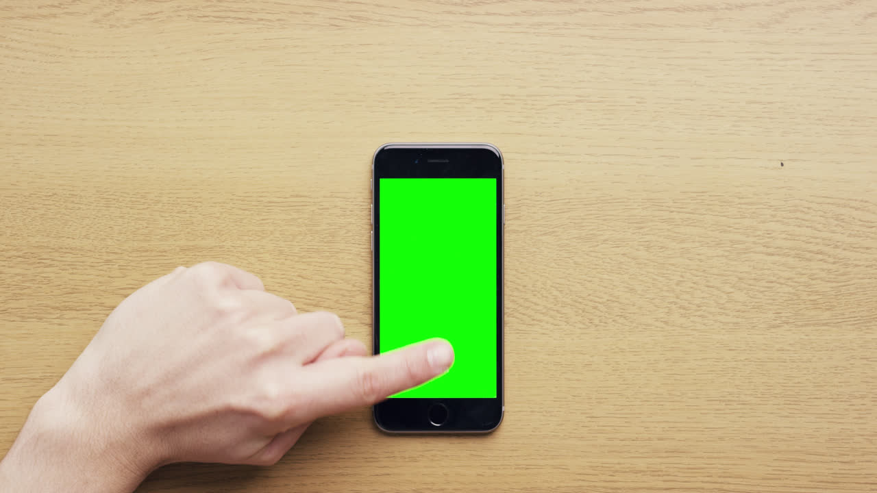 Vista dall'alto: mani che usano un telefono cellulare touchscreen con gesti multi-touch su schermo verde, su una scrivania in legno - Red Epic Dragon