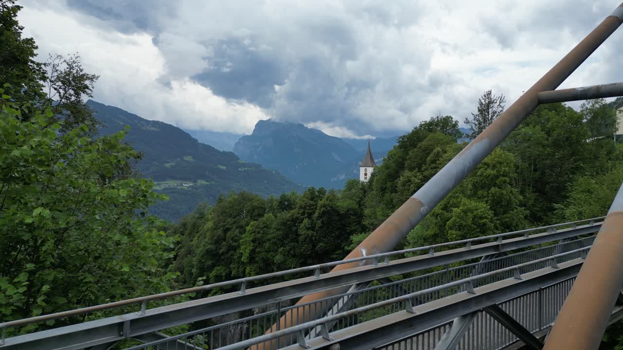 primer plano del puente colgante con el campanario de la iglesia en el horizonte con la naturaleza alpina