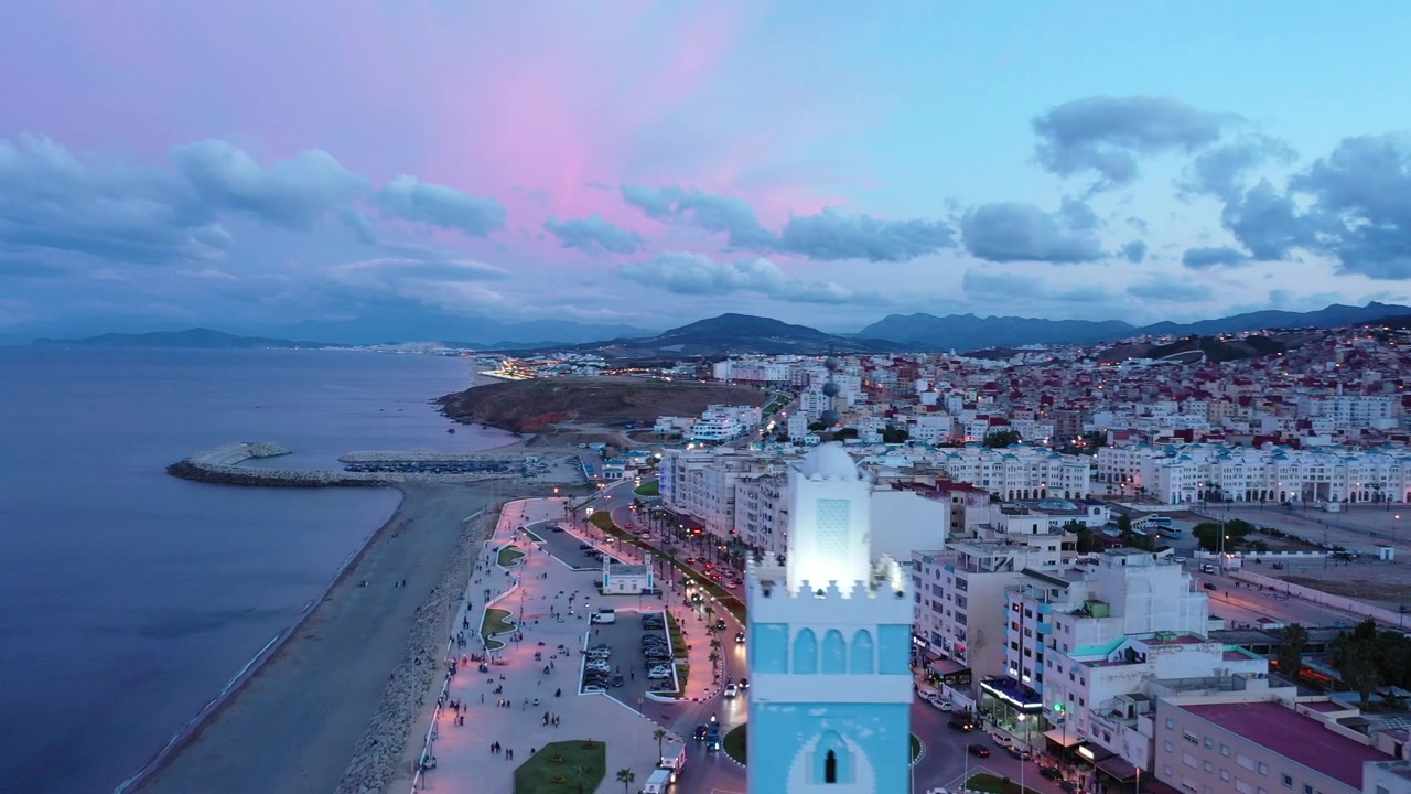 Vista de drone na hora azul de M'diq na costa mediterrânea de Marrocos, apresentando a Mesquita dos Sete Homens, calçadão à beira-mar e paisagem urbana costeira no Norte de Marrocos, Norte da África