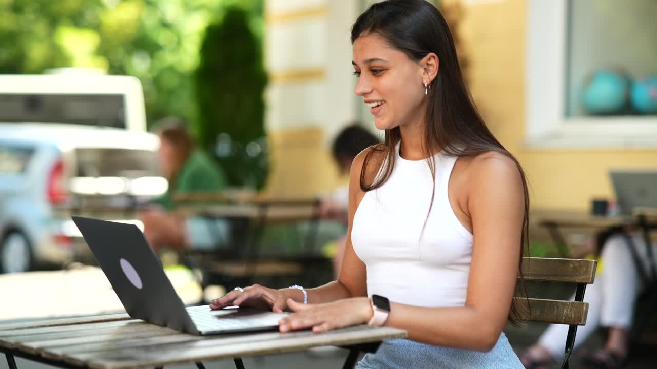 mujer joven trabajando en una computadora portátil en un café al aire libre