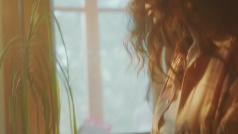 curly-haired girl spraying houseplant with water in sunlit room