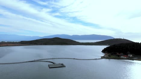 Beautiful-seaside-with-island-full-of-pine-trees-forest,-wooden-piers-on-shallow-lagoon-reflecting-cloudy-sky-in-Zvernec,-Albania