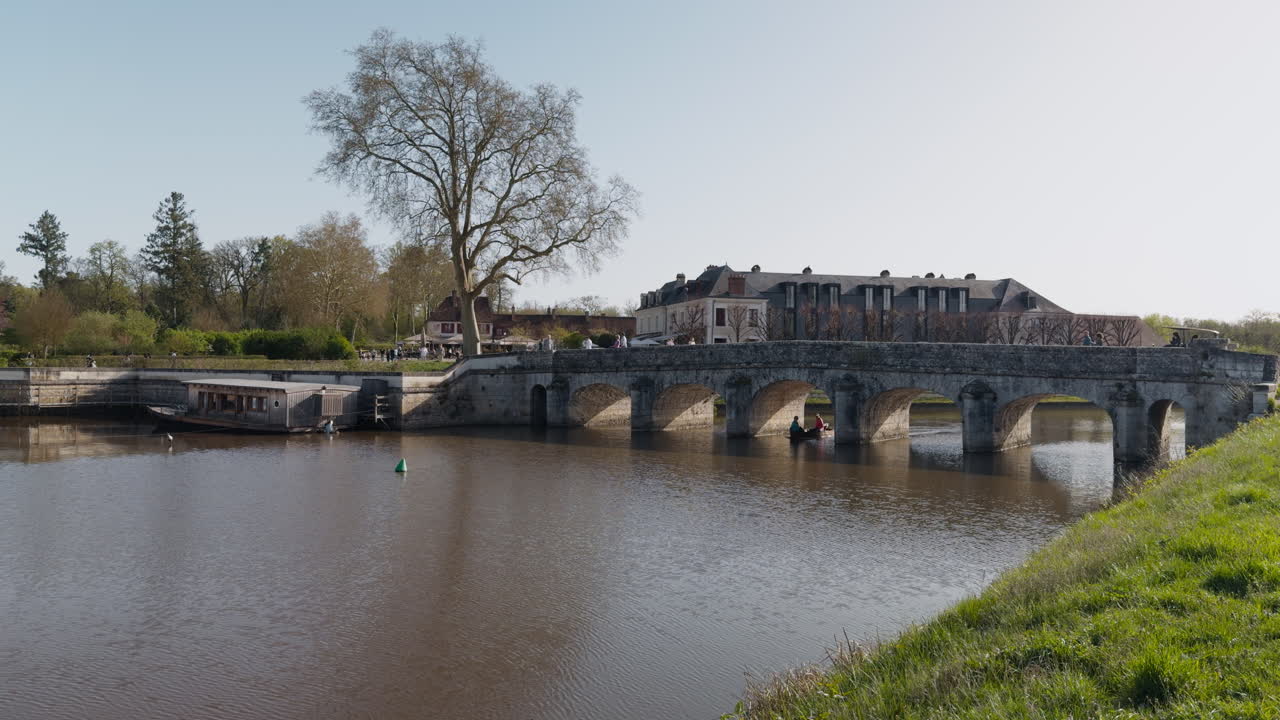 Historic stone bridge over Le Cosson near Château de Chambord, spring day, tourists walking