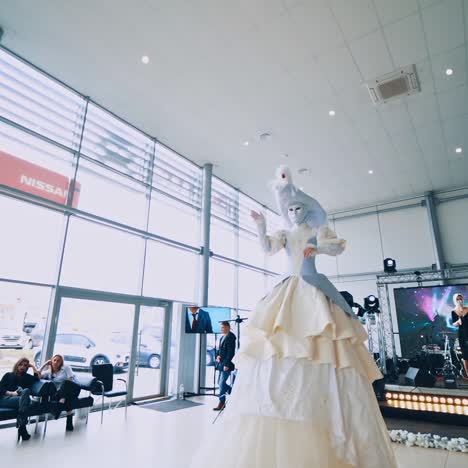preparation for the show. tall woman in mask and white dress moving in the hall. singer is singing on stage. empty chairs in the room.