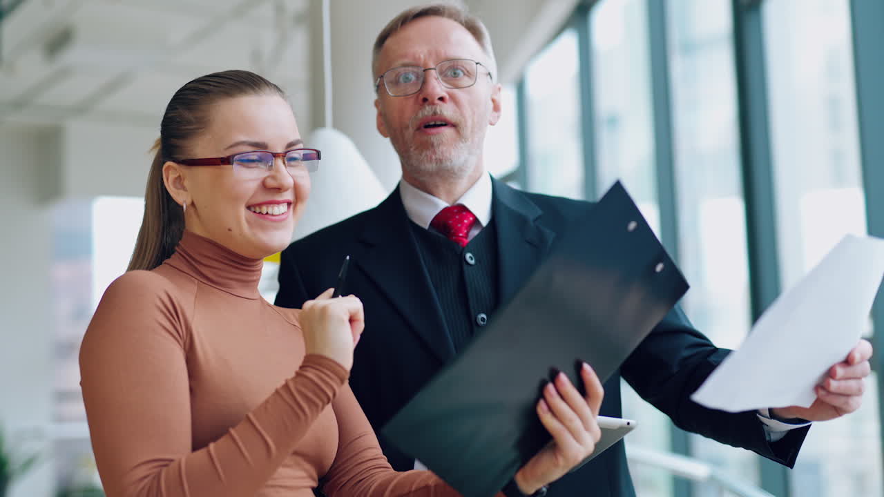 Colleagues are talking about the company. Smiling young secretary shares her ideas with a senior businessman inside the office. Business concept.