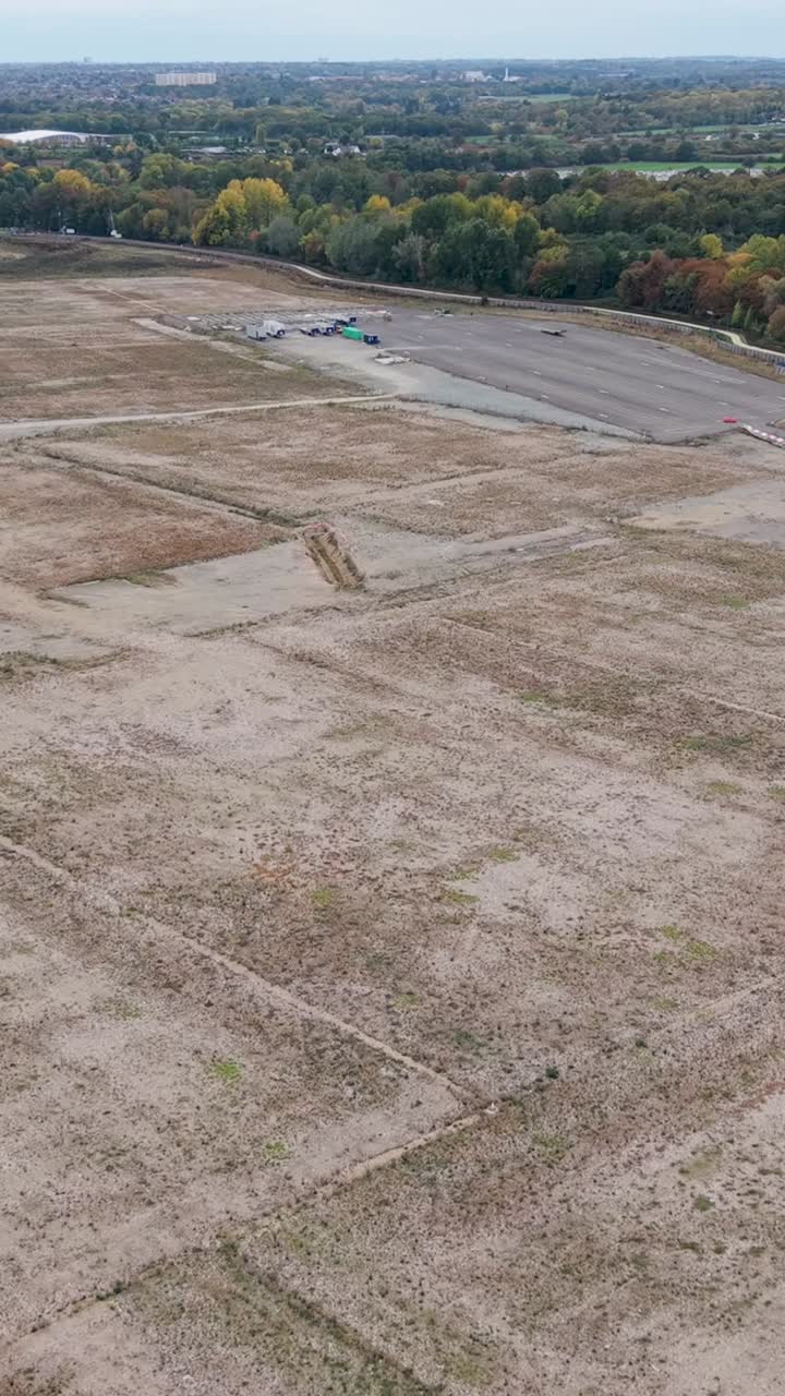 Vertical high drone view over the former site for Sunset Studios in Waltham Cross, Hertfordshire. The shot captures empty land, blue hoarding, autumn trees, and the busy A10 road junction below