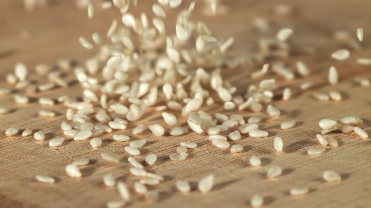 Semi di sesamo bianchi che cadono su una superficie di legno al rallentatore