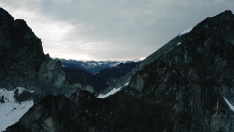 Alaskan-Rugged-Mountain-Range,-Drone-Flying-through-the-Clouds-and-over-a-ridge-in-the-Mountains-at-Sunrise