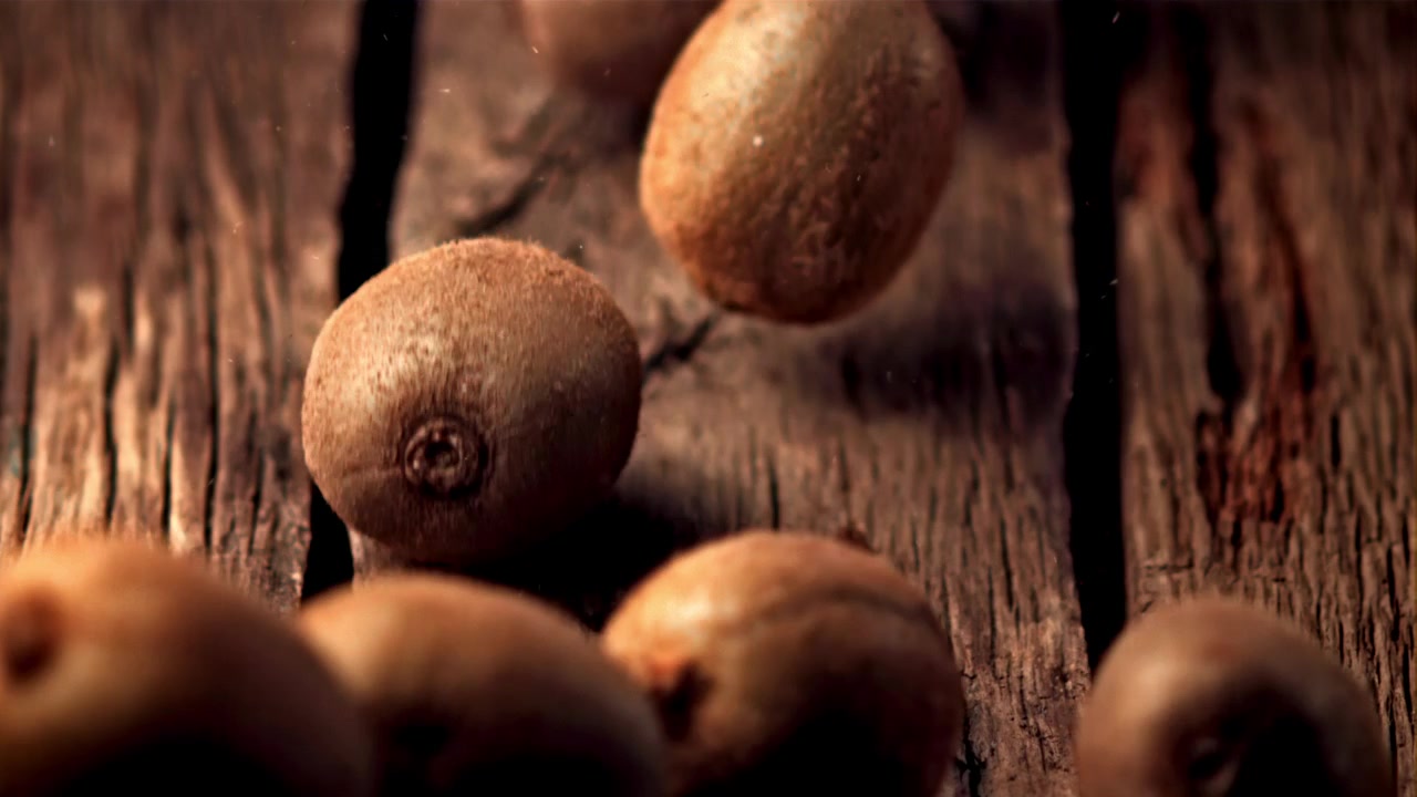 Kiwi freschi che cadono su un tavolo di legno rustico al rallentatore.