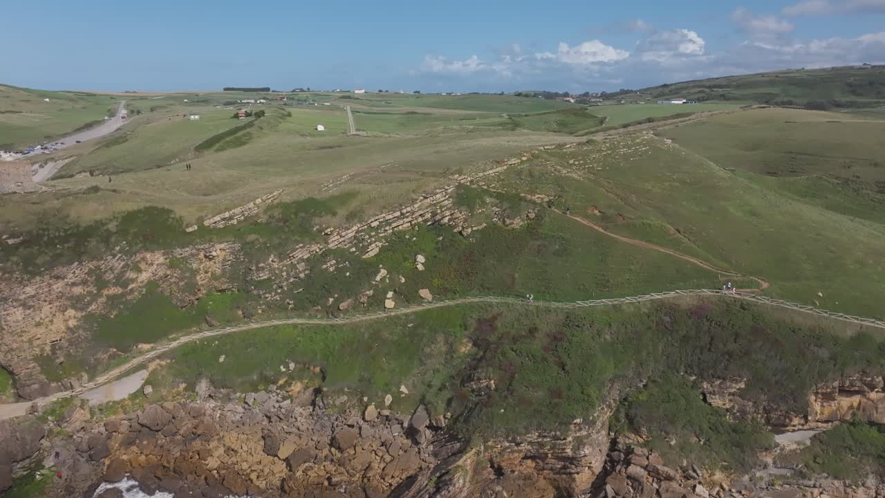 Drone flight descending over Cantabrian rolling green meadows towards the turquoise coast at 24fps in slow motion. The scene reveals peaceful rural landscapes meeting the wild northern sea